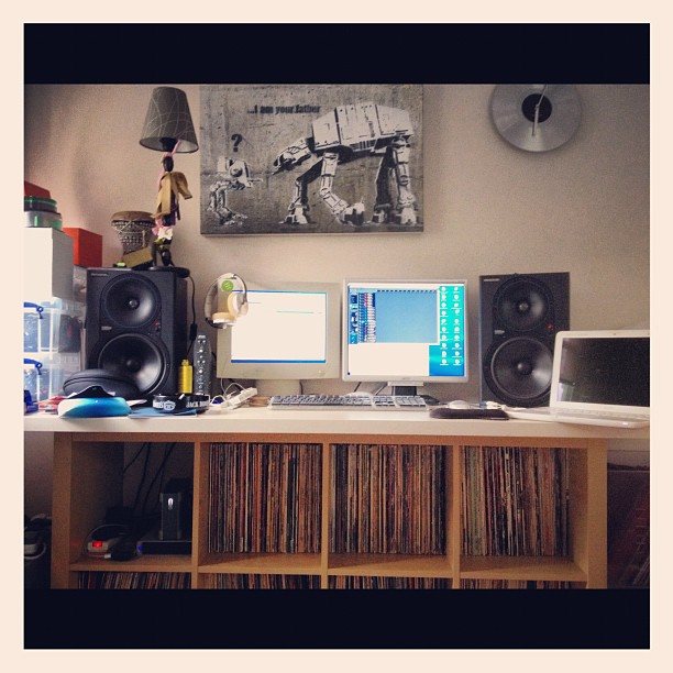Studio desk with two monitors and speakers above shelves of vinyl