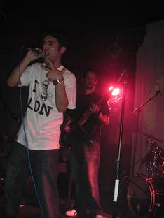An MC in an I love LDN t-shirt on stage with a bassist behind him under red light