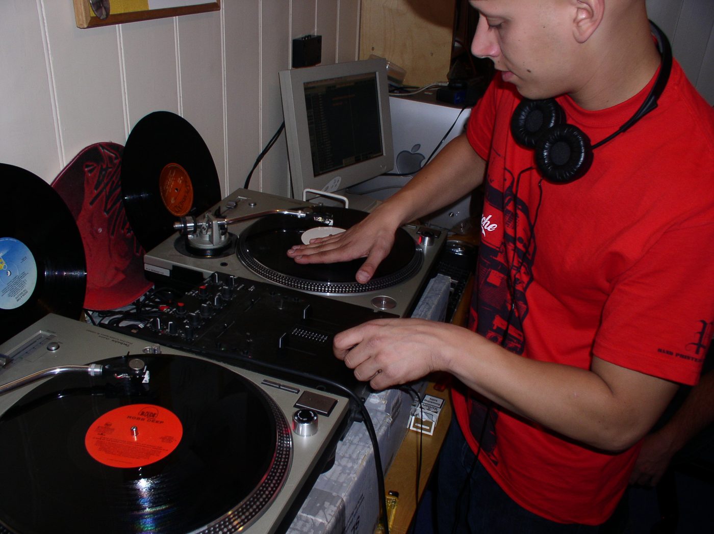 A member in a red shirt with a hand on the platter, two turntables and a mixer