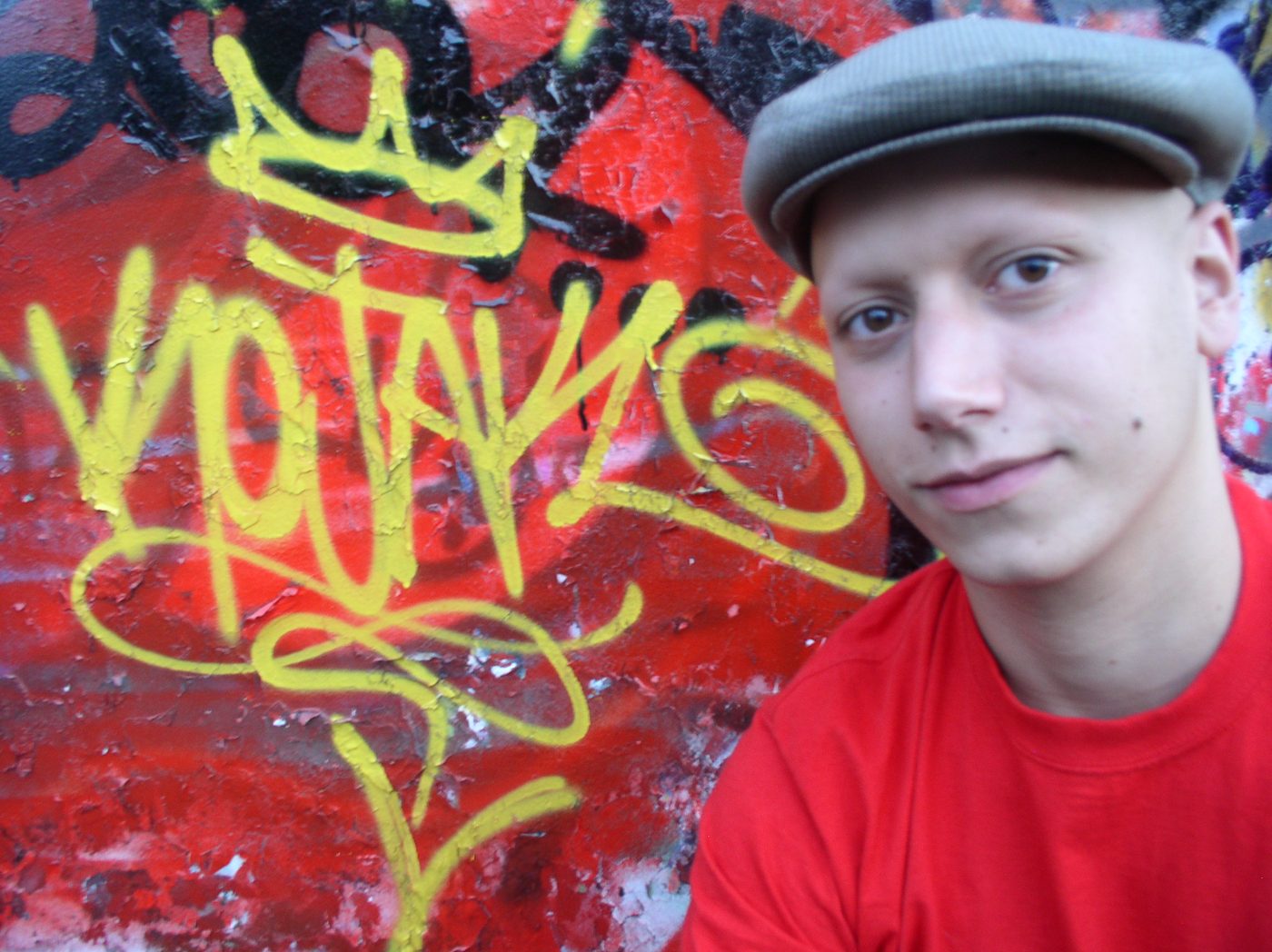 Close-up portrait in a flat cap and red shirt beside a yellow tag
